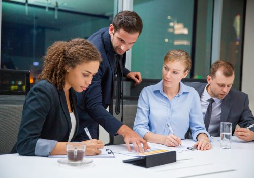 Business people sitting in conference room and discussing business issues. Executive manager standing, pointing to document and explaining his idea to business team